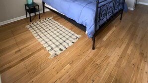 Una camera da letto con un letto, un comodino, una decorazione macramè appesa al muro e un pavimento in legno.