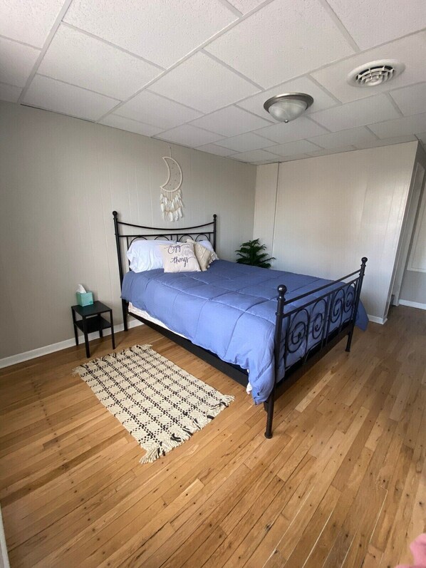 A bedroom with a bed, a nightstand, a wall-mounted macrame decoration, and a wooden floor.
