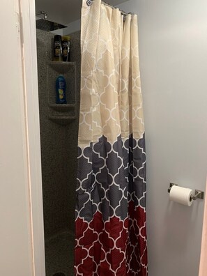 Ein Badezimmer mit Duschvorhang mit geometrischem Muster, einem Handtuchhalter mit Pflegeprodukten und einem Toilettenpapierhalter.