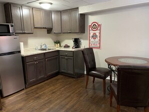 A compact kitchen with dark cabinets, a stainless steel refrigerator, a microwave, a coffee maker, and a dining table with chairs. - 1 Bedroom Apartment in Downtown Coshocton (23) (Coshocton)