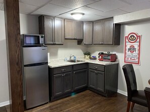 A compact kitchen with dark cabinets, a stainless steel refrigerator, a microwave, and a red toaster oven. - 1 Bedroom Apartment in Downtown Coshocton (23) (Coshocton)