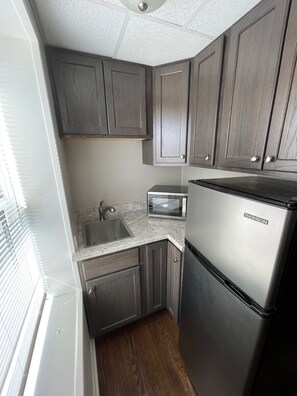 A compact kitchen with dark wood cabinets, a stainless steel refrigerator, and a built-in oven. - Studio Apartment on Main Street in Coshocton (35) (Coshocton)