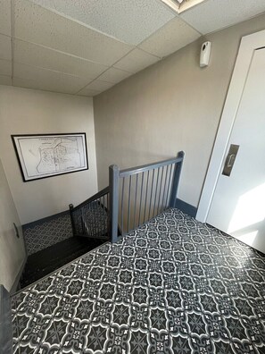 A staircase with patterned floor tiles, a metal railing, and a framed map on the wall. - Studio Apartment on Main Street in Coshocton (35) (Coshocton)