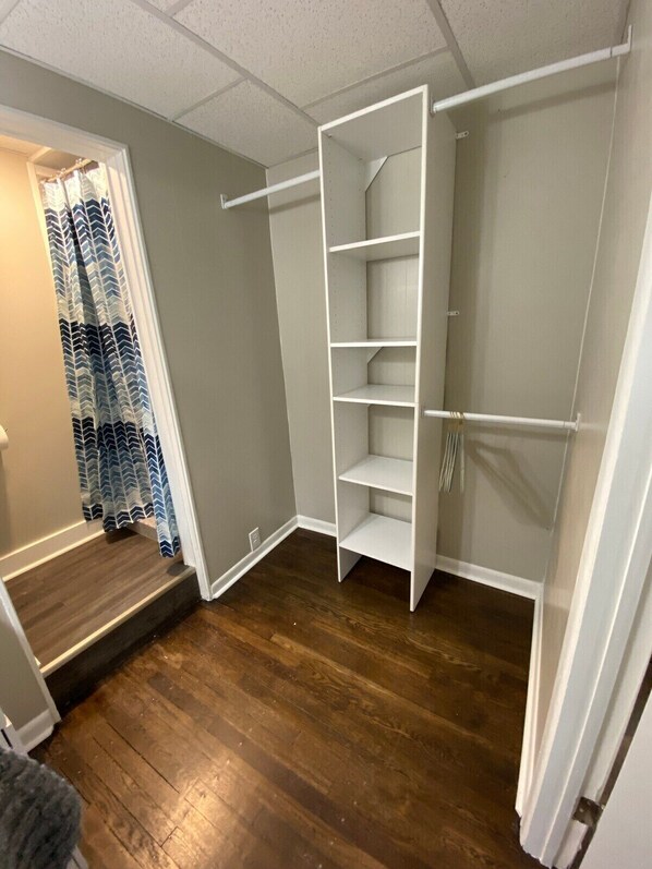 A walk-in closet with open shelving and a hanging rod, wooden flooring, and a patterned curtain.