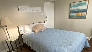 A bedroom with a bed, a nightstand, a lamp, a painting, and a motivational quote on the wall. - Studio Apartment on Main Street in Coshocton (36) (Coshocton)