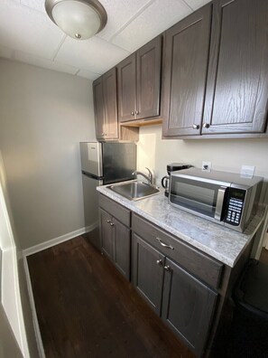 Una cocina compacta con armarios de madera oscura, un refrigerador de acero inoxidable, un microondas y un lavabo.