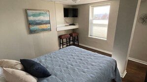 Ein Schlafzimmer mit Bett, einem an der Wand montierten Fernseher, einem Fenster mit Blick und einem Gemälde.
