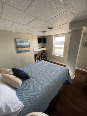 A bedroom with a bed, a TV mounted on a wall, a window with a view, and a painting on the wall.