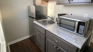 A compact kitchen with dark wood cabinets, a stainless steel refrigerator, a microwave, and a sink. - Studio Apartment on Main Street in Coshocton (26) (Coshocton)