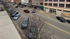 A street view with parked cars, buildings, and a clear sky. - Studio Apartment on Main Street in Coshocton (26) (Coshocton)