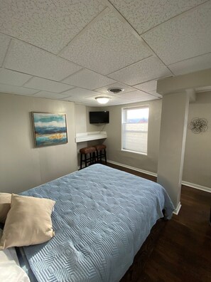 A bedroom with a bed, a painting, a television, and a window. - Studio Apartment on Main Street in Coshocton (26) (Coshocton)