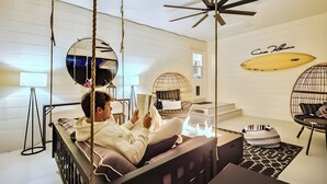 A modern living room with a swing chair, a ceiling fan, and a surfboard decoration.