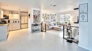 A modern living space with a kitchen, a seating area with a sofa and armchairs, and a wall decorated with framed pictures.
