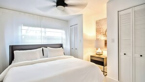 A modern bedroom with a large bed, a ceiling fan, a bedside table with a lamp, and a wardrobe.