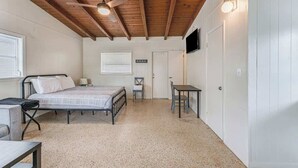 A bedroom with a bed, a desk, a chair, a ceiling fan, and a TV mounted on the wall. - Cozy River Cabin | Escape to Seven Sisters Springs (Homosassa)