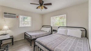 Ein Zimmer mit zwei Betten, einem Deckenventilator, einer Klimaanlage und einem Fenster mit Jalousien.