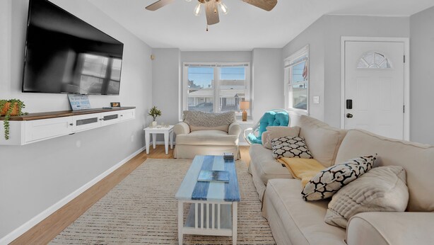 A living room with a flat-screen TV, a ceiling fan, a sofa, a coffee table, and a window with a view.