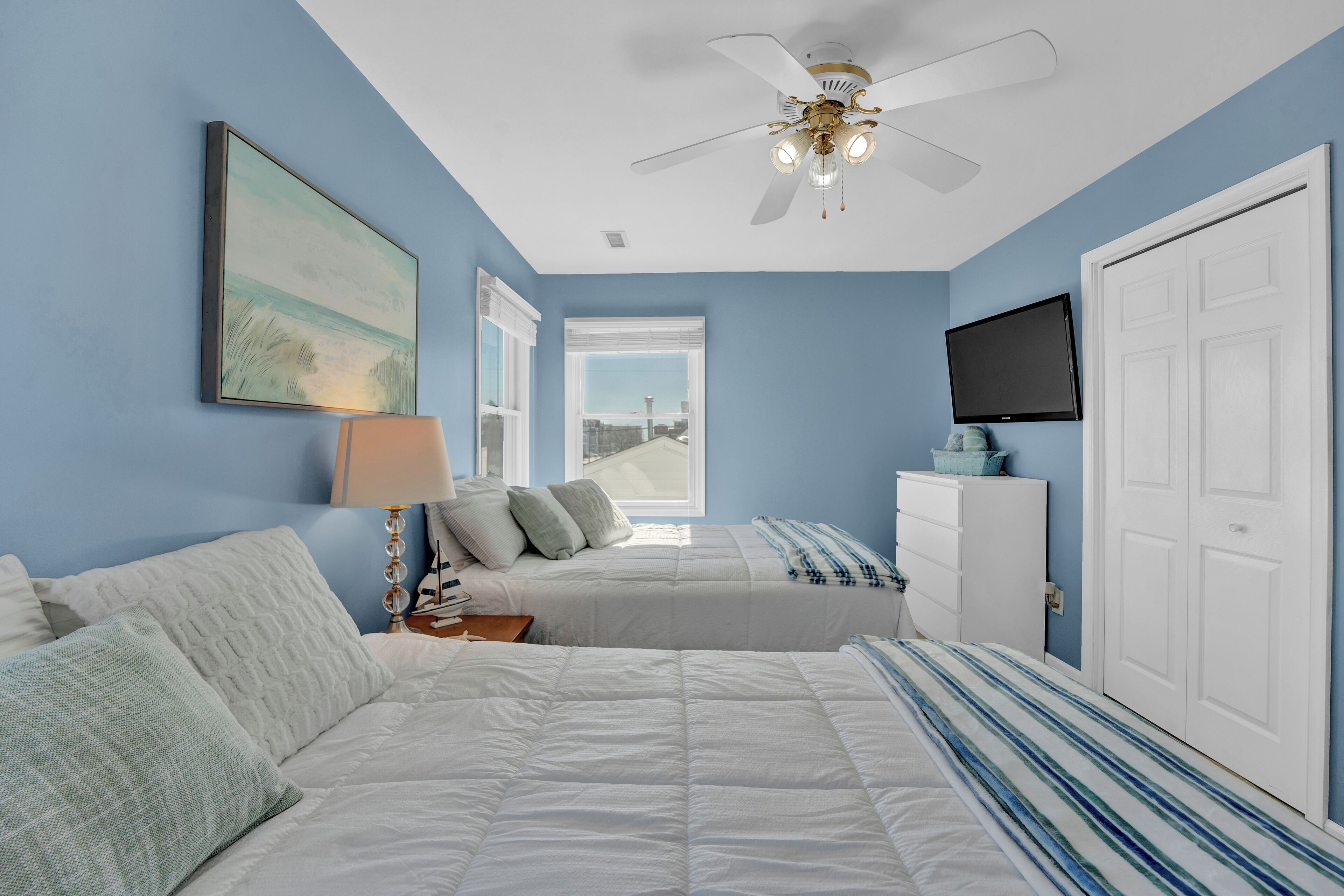 A bedroom with two beds, a ceiling fan, a TV, and a window with a view.