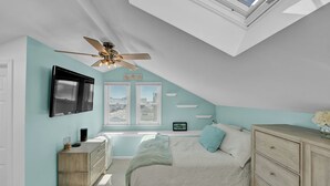 A bedroom with a skylight, a ceiling fan, a bed, a dresser, and a television.