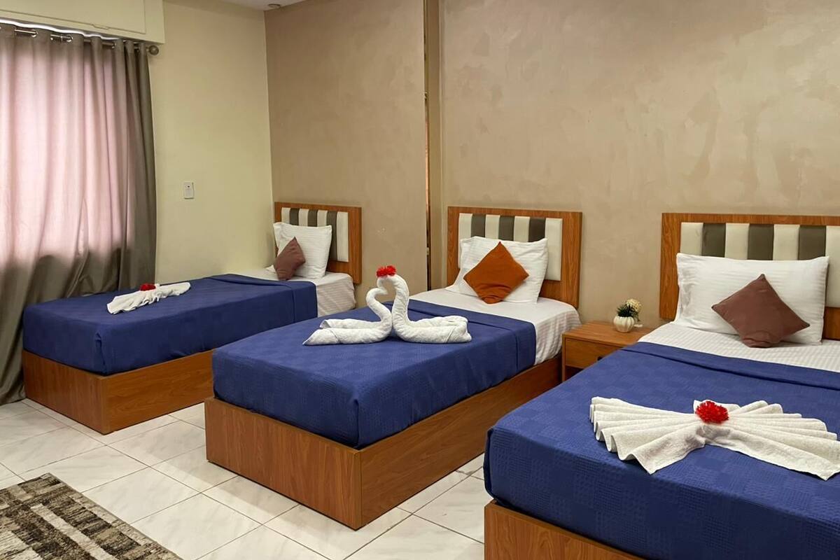 Une chambre d’hôtel avec trois lits, chacun recouvert d’une couverture bleue et agrémenté d’une serviette en forme de cygne.