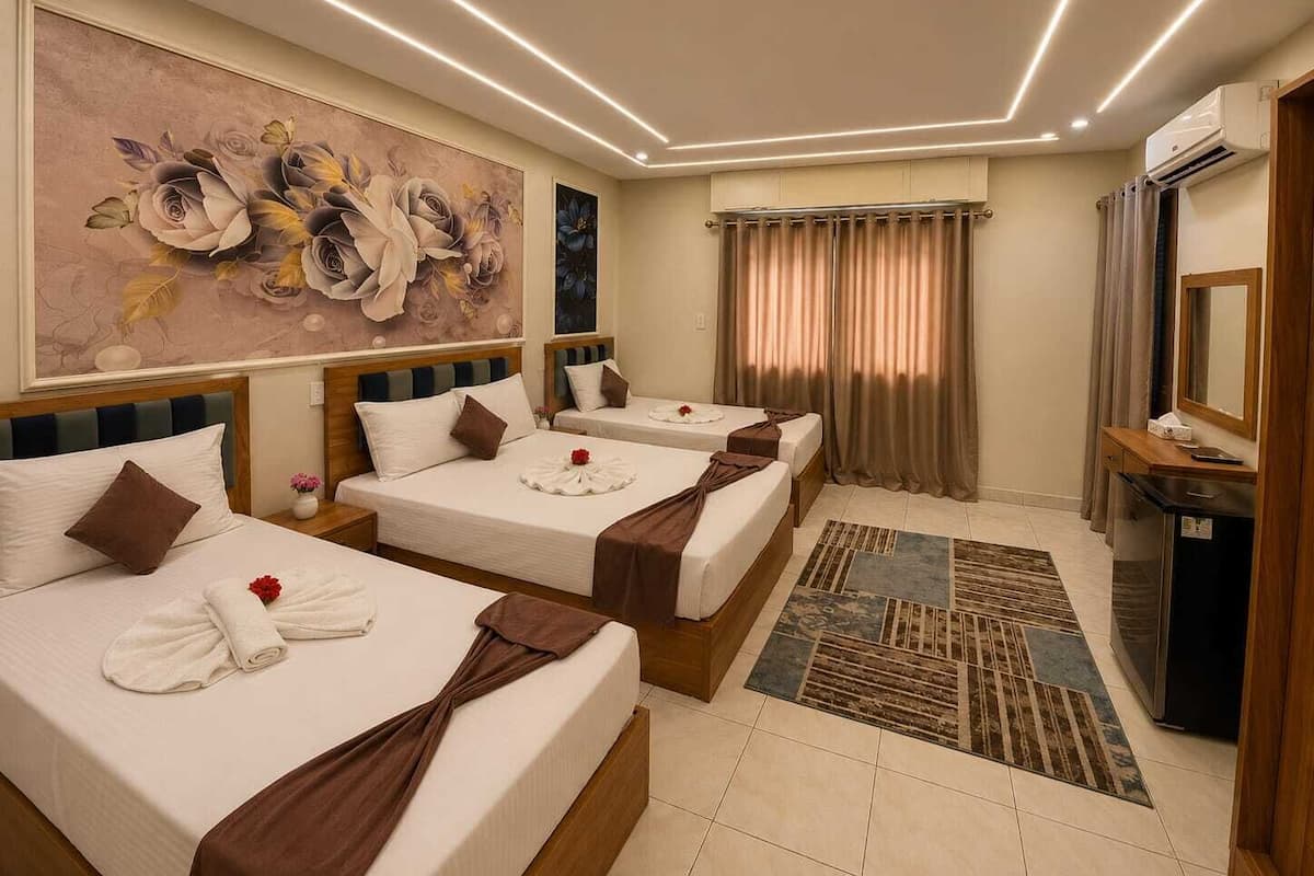 Une chambre d’hôtel avec trois lits, un grand tableau représentant des fleurs, un appareil de climatisation et un bureau avec un miroir.
