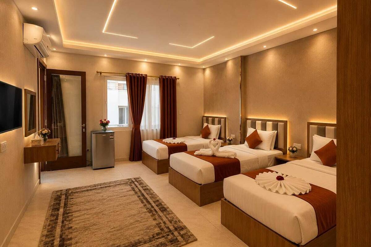 Une chambre d’hôtel avec trois lits, une télévision, un minibar et un grand tapis.