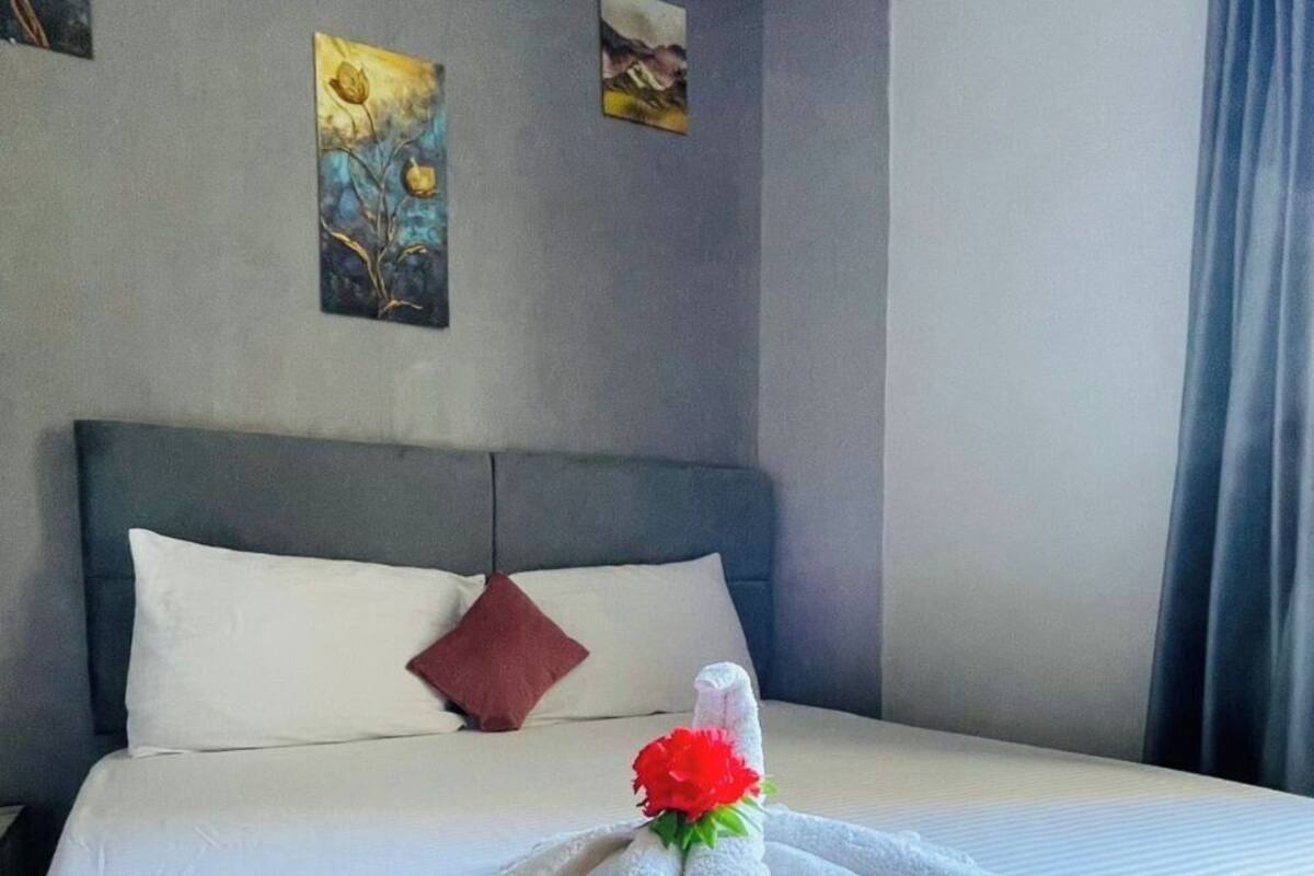 Un lit bien fait, agrémenté d’une serviette et d’un bouquet de fleurs rouges, une tête de lit grise et deux tableaux accrochés au mur.