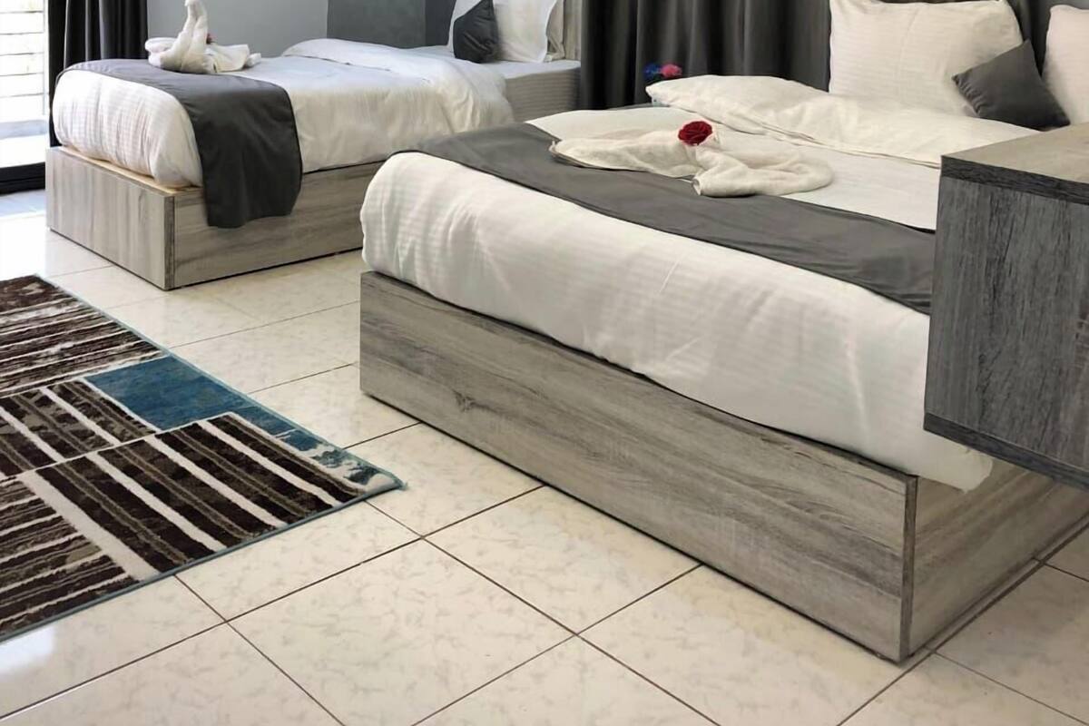 Une chambre d’hôtel moderne avec deux lits, une grande fenêtre avec des rideaux, une tête de lit en bois et un tapis à motifs.