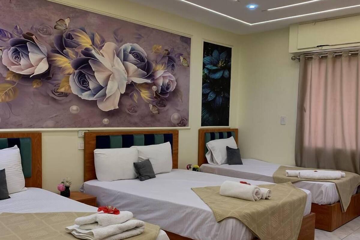 Une chambre d’hôtel avec trois lits, une grande fresque murale à motifs floraux et un tapis à motifs.