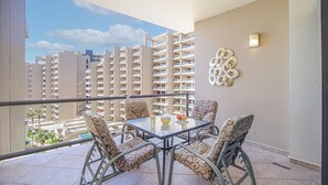 Ein Balkon mit Glastisch, vier Sitzgelegenheiten mit Muster, einer Wanddekoration und Blick auf Hochhäuser.