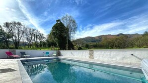 A rectangular swimming pool with clear blue water, surrounded by a stone wall and a paved deck. There are three lounge chairs with cushions, and a large tree is visible in the background. - KURUTXETA - LASSE - Gîte (LASSE)