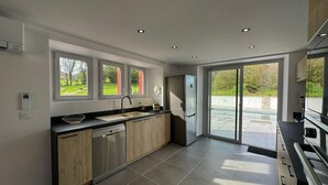 A modern kitchen with a dishwasher, a refrigerator, and a large window overlooking a garden. - KURUTXETA - LASSE - Gîte (LASSE)