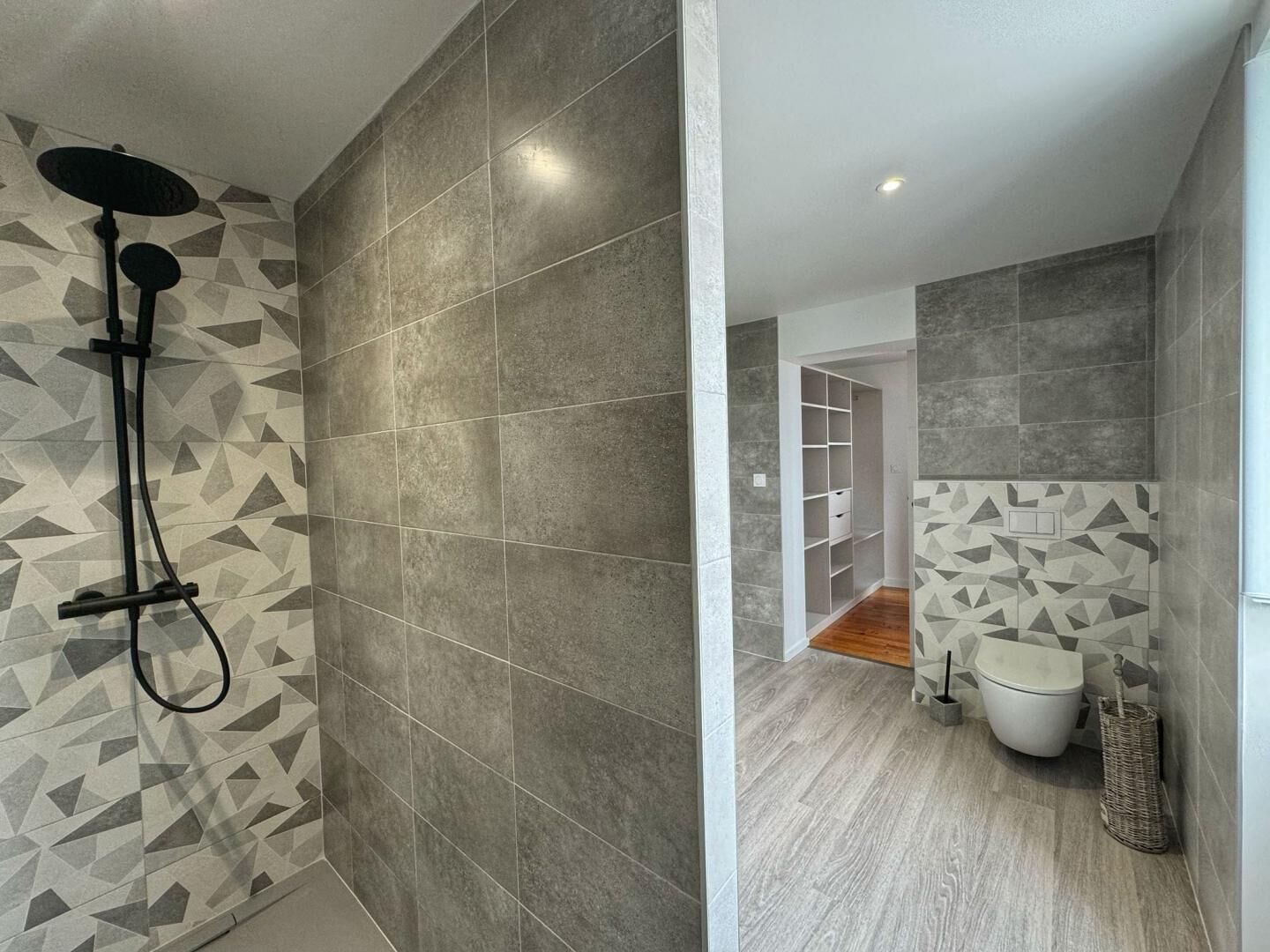 A modern bathroom with a shower, tiled walls, and a wooden floor.