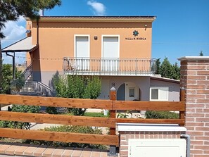 Un bâtiment à deux étages appelé « Villa N. Nigola », doté d’un balcon, d’un escalier et d’un mur en briques.