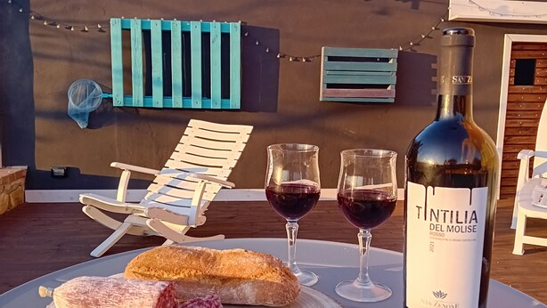 A table with a bottle of wine, two glasses, a baguette, and salami on a wooden board.