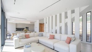 Una sala de estar moderna con un sofá modular, dos mesas redondas de centro y una cocina al fondo.