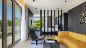 A modern living room with a sofa, a chair, and a coffee table. There is a large window with curtains, a painting on the wall, and a view of the outdoors. - Das Affalterbach, Stuttgart, Autograph Collection (Affalterbach)