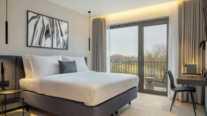 A modern hotel room with a large bed, a desk, and a view of the outdoors through a sliding glass door. - Das Affalterbach, Stuttgart, Autograph Collection (Affalterbach)