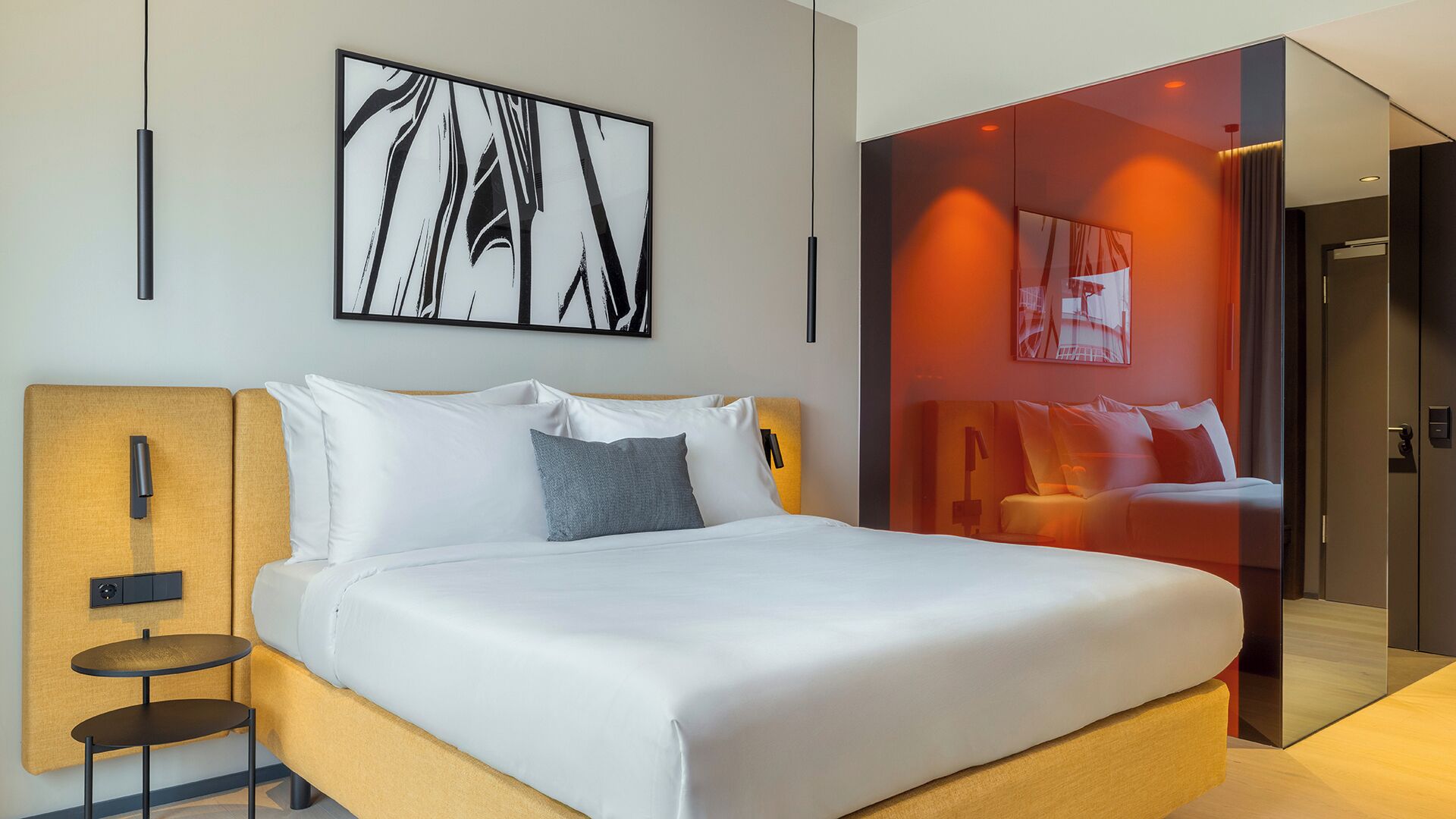 Una habitación de hotel moderna con cama, mesita de noche, una obra de arte en la pared y un separador de vidrio.