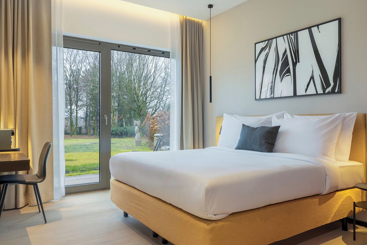 Habitación de hotel moderna con una cama grande, un escritorio y vistas a un jardín a través de una puerta corredera.