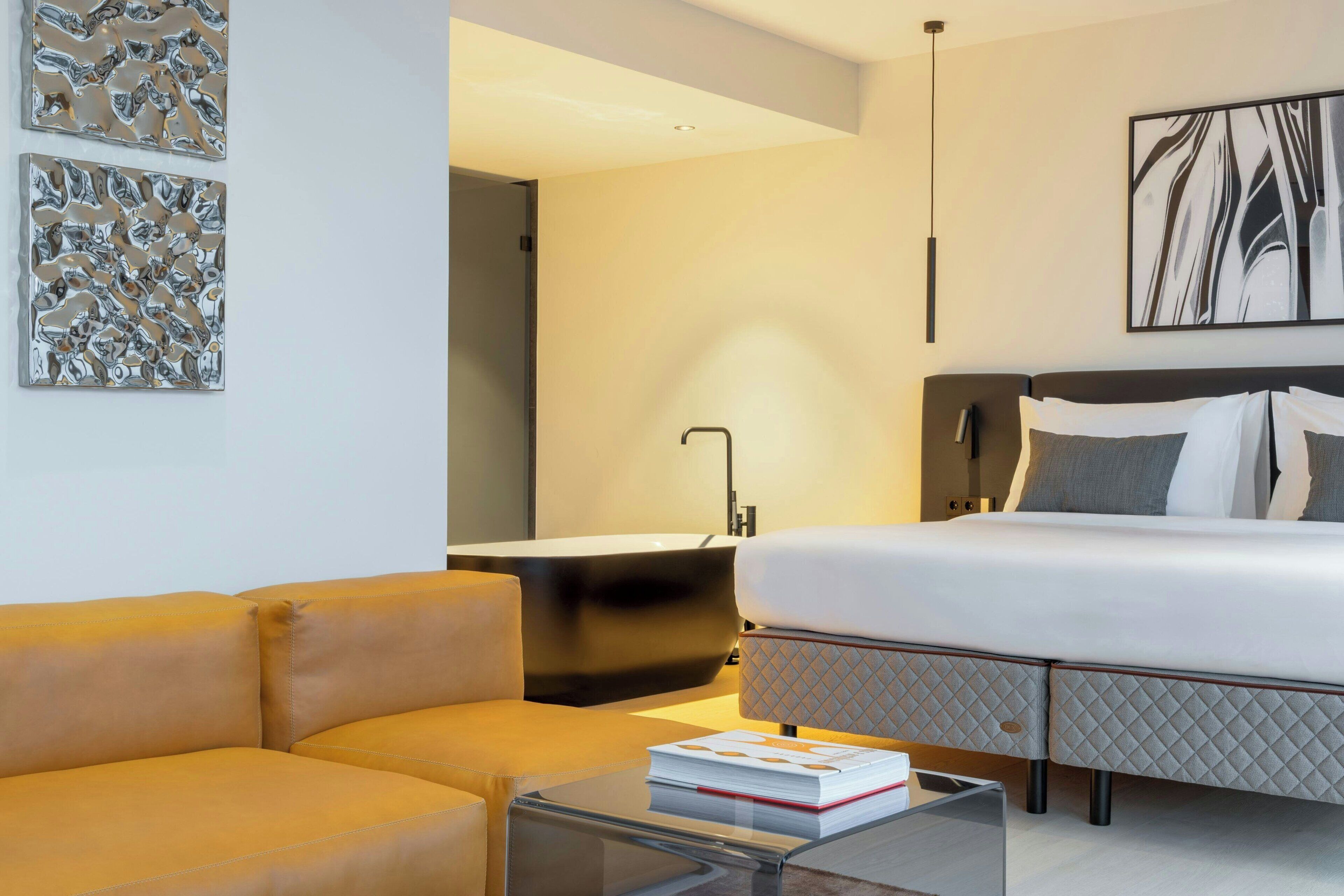 Een moderne hotelkamer met een bed, een sofa, een bijzettafeltje en kunstwerken aan de muur.