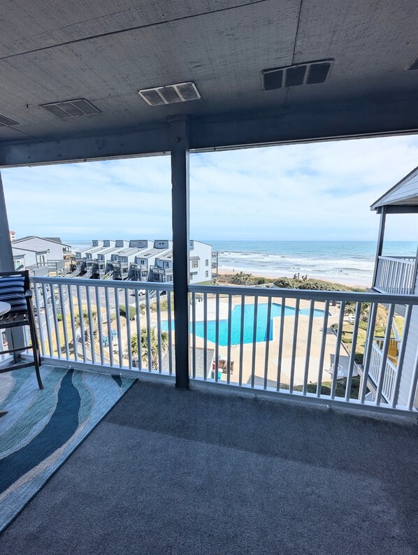 A balcony with a view of the ocean, a pool, and a building complex.