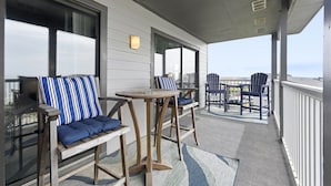 A covered outdoor seating area with wooden chairs and tables, a view of the ocean, and a railing along the edge. - Clean, Oceanfront Condo w/ Pool Access, King Suite, Bunks & Beautiful Views! (North Topsail Beach)