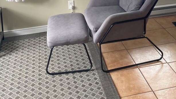 Una sala de estar moderna con un sillón gris, una alfombra estampada, un cuadro de un lago y una ventana con vistas a colinas nevadas.