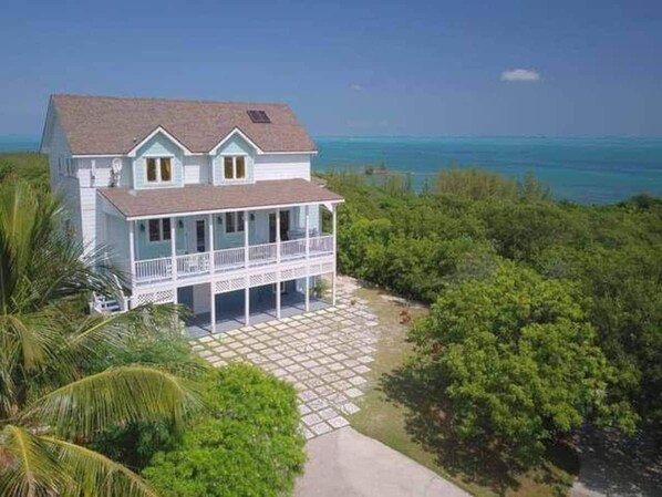 A two-story house with a balcony, surrounded by lush greenery and a view of the ocean.