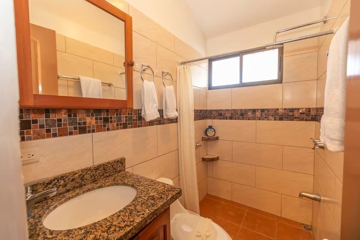 Une salle de bain avec un lavabo en granit, un miroir, une douche et une fenêtre.