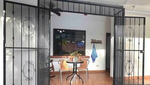 A gated entrance with a 'Welcome' sign, a small patio with a table and chairs, and a window with a view. - Poolside in Paradise: Walk to the Beach and More! (Coco)