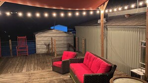 Een overdekt terras buiten, met rieten meubels en lichtslingers.