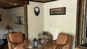 Een gezellige kamer met twee rieten stoelen, een ronde tafel, een open haard en rustieke decoratie, waaronder een welkomstbord.