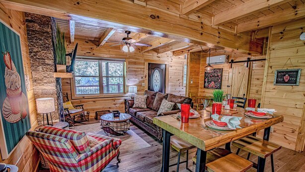 L’intérieur chaleureux d’un chalet avec une table à manger en bois, préparée pour quatre personnes, un canapé et un fauteuil coloré.